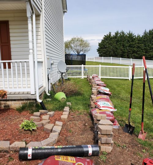 Tilling and extending existing garden bed to wrap around the house with stone wall and landscape fabric